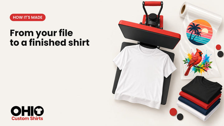 A heat press, a roll of transfer film with colorful printed designs and a stack of folded T-shirts